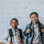 Focused multiracial children in casual outfits with backpacks standing in classroom against whiteboard at school and looking at camera