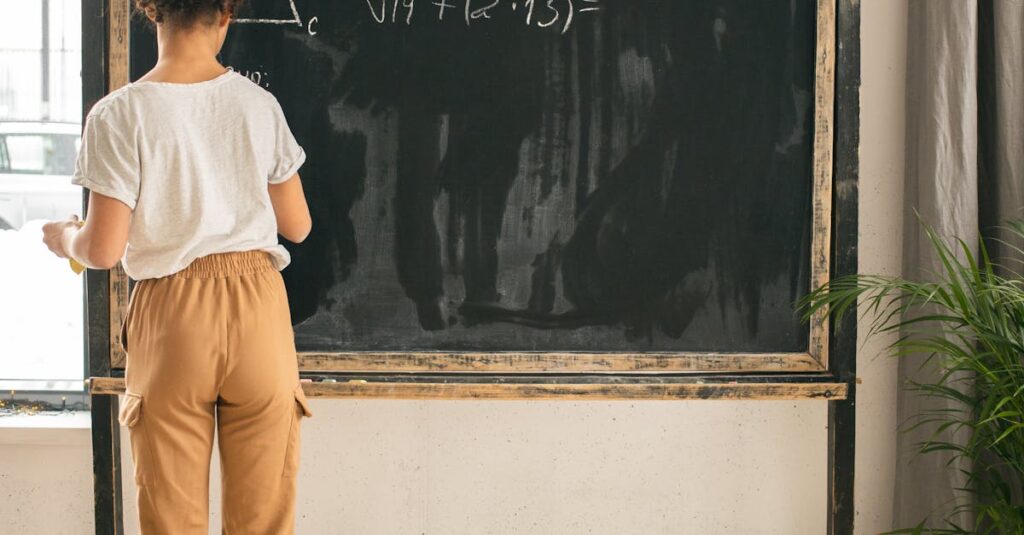 Back view full body of clever faceless girl writing on blackboard while solving mathematical equation during lesson in light room