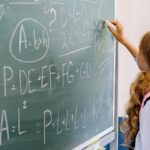 Young girl student writing math equations on classroom blackboard during a lesson.
