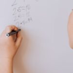 A young girl solving math problems on a whiteboard indoors, showcasing education and learning.